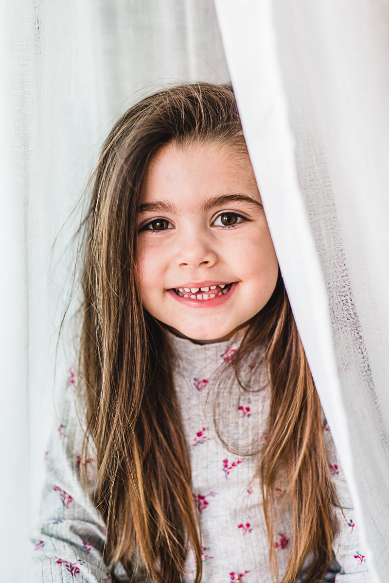 Close up portrait of a little girl in white curtain in Dorset