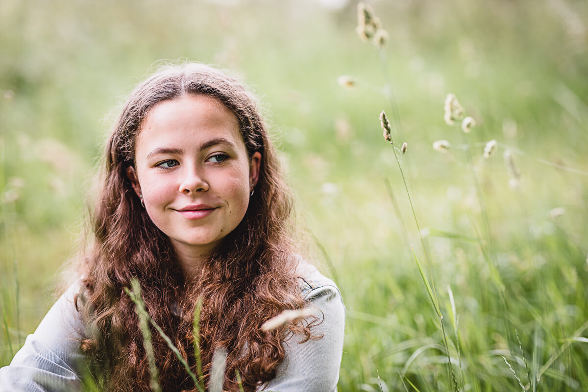 Young girl sitting in long grass captured by Dorset Portrait Photographer