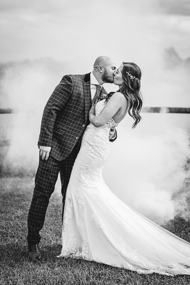 Bride and Groom kissing whilst surrounded by white smoke