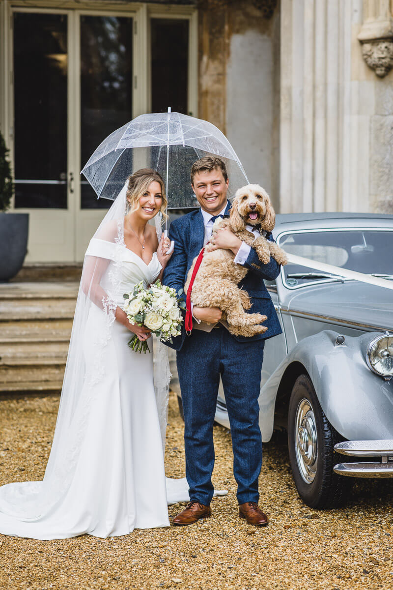 Bride and Groom under an umbrella with there dog outside Highcliffe Castle