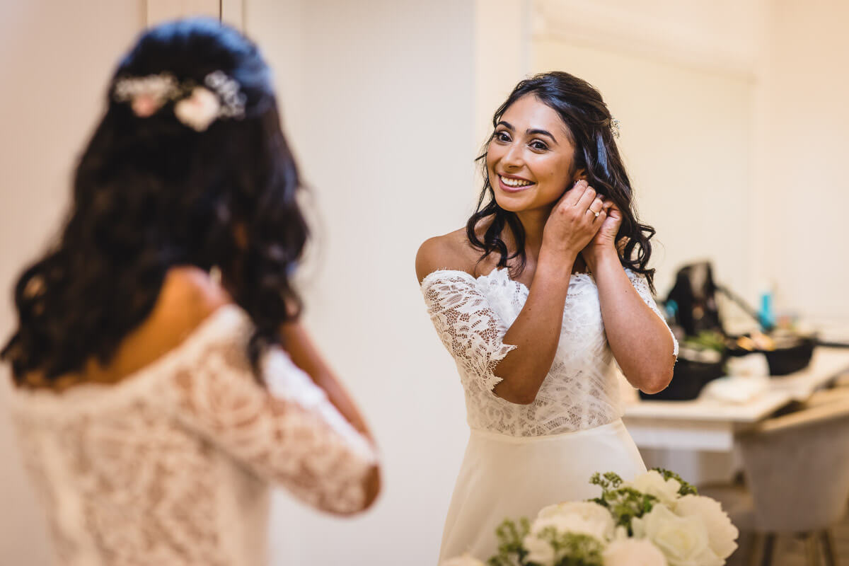 Bride looking in the mirror putting her earrings on in the getting ready room at Crowcombe Court